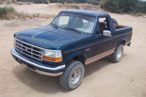 1995 Ford Bronco - Dark teal 1995 Ford Bronco with tan trim and spare tire visible in rear.