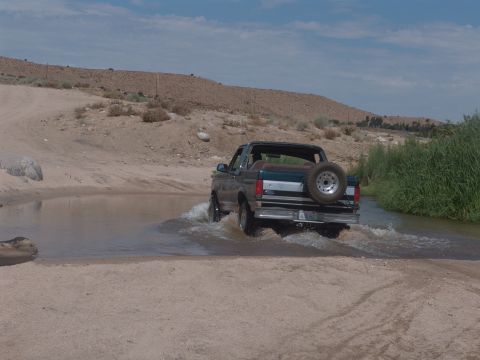 1995 Ford Bronco - A Ford Bronco navigates a water crossing in a dry, desert landscape.