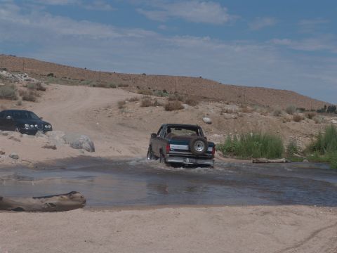 1995 Ford Bronco - A 1995 Ford Bronco navigates a shallow stream in a desert landscape, with another vehicle visible in the background.