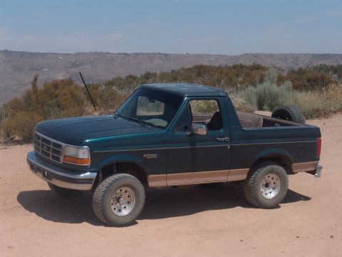 1995 Ford Bronco - This 1995 Ford Bronco is shown in a three-quarter front view, parked on a dirt road with arid hills in the distance.