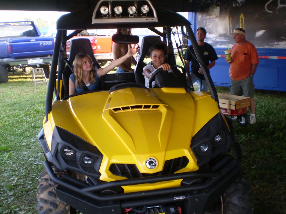 Yellow ATV with black roll cage and seats, front view. Two girls are inside