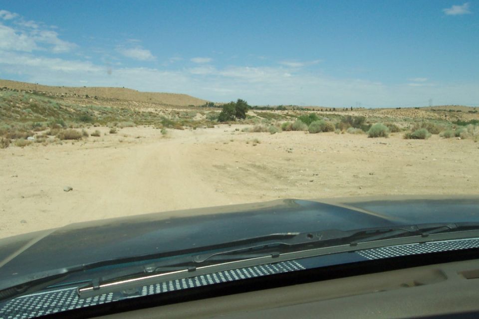 View of a dirt road through a desert landscape, seen from inside a vehicle. A watermark reads SUPERMOTORS