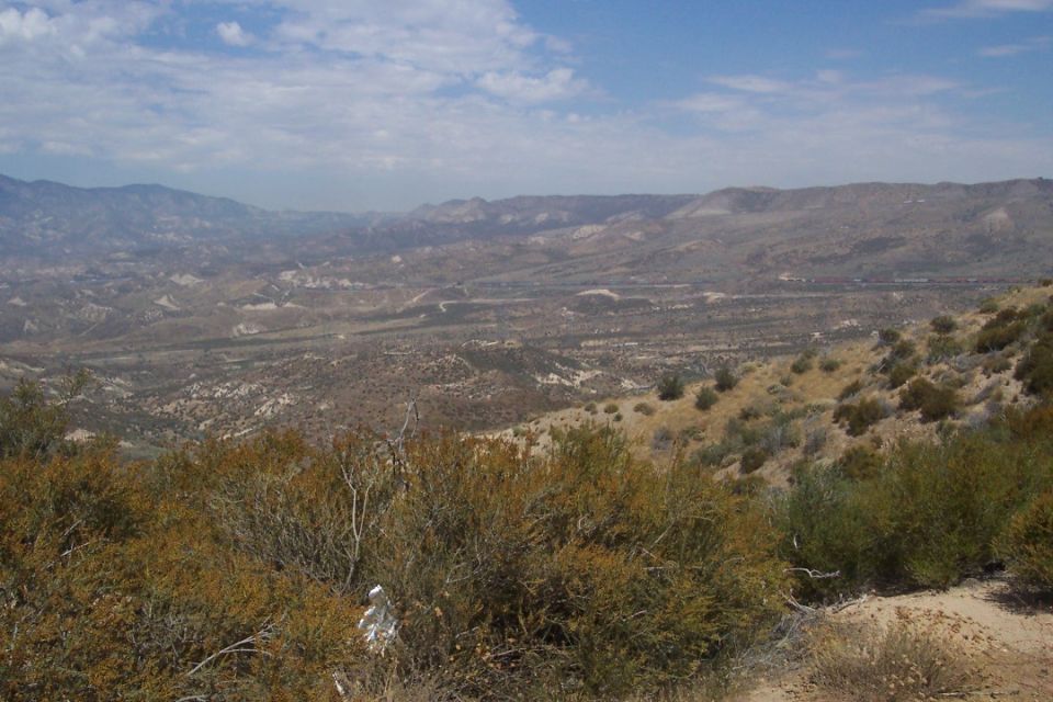 Desert landscape with mountains in the distance and scrub brush in the foreground. Watermark reads SUPERMOTORS