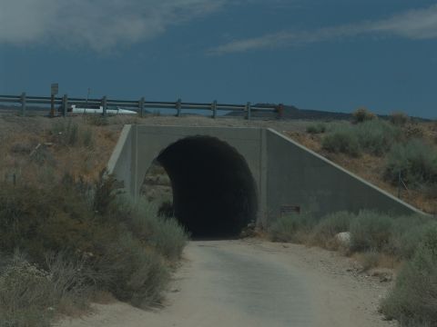 1995 Ford Bronco - A white vehicle is parked on the side of the road above a tunnel entrance in a dry, brushy landscape.