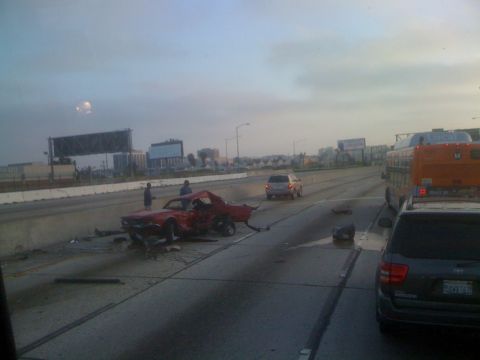 1968 Ford Mustang - A severely damaged red coupe sits on the highway shoulder after an apparent accident.