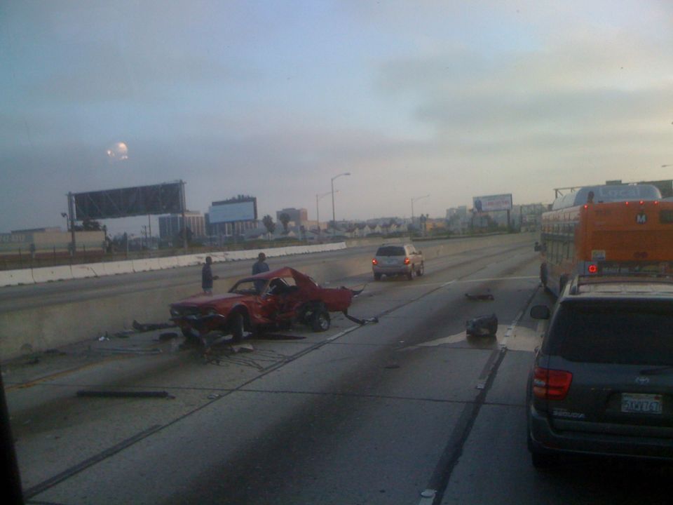 Red 1967 Ford Mustang coupe, heavily damaged, on highway shoulder