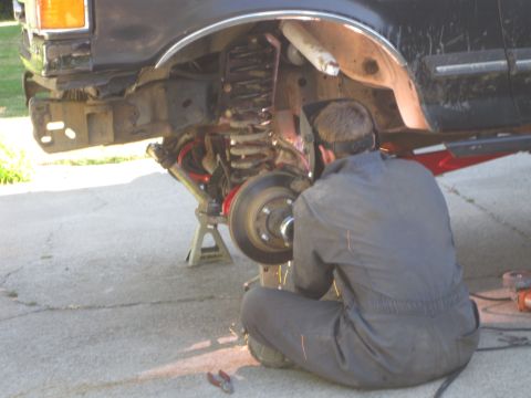 1989 Ford Bronco - Mechanic performs work on the front suspension of a black SUV.