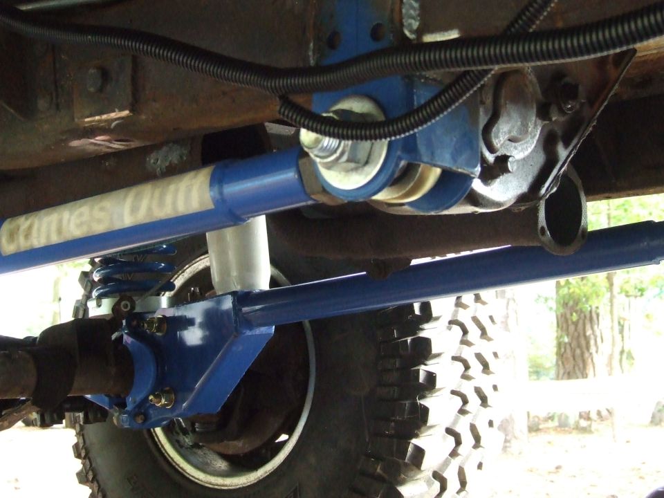 Close-up of blue suspension parts on a vehicle, with a tire visible. Text on a blue bar reads "Crites Out"