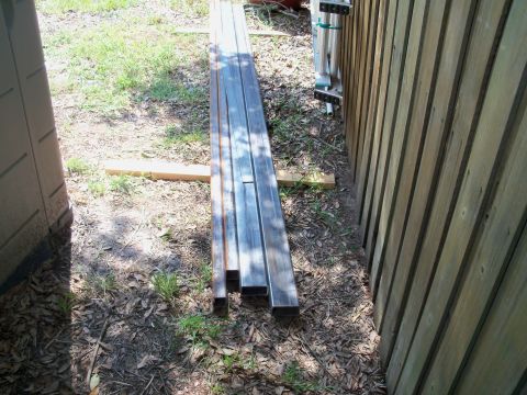 1978 Jeep CJ5 - Metal pipes are stored outdoors next to a wooden fence and a plastic storage shed.