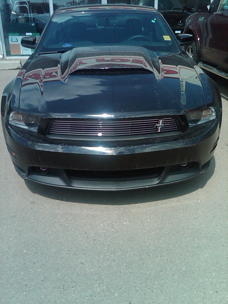 Black Ford Mustang with a prominent hood scoop and horizontal grille, viewed from the front