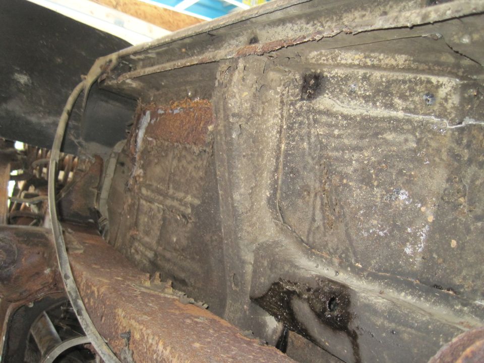 Undercarriage of a heavily rusted vehicle, showing frame damage and corrosion