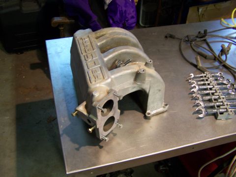1989 Ford Bronco - A Ford intake manifold is shown on a workbench next to tools and engine parts.