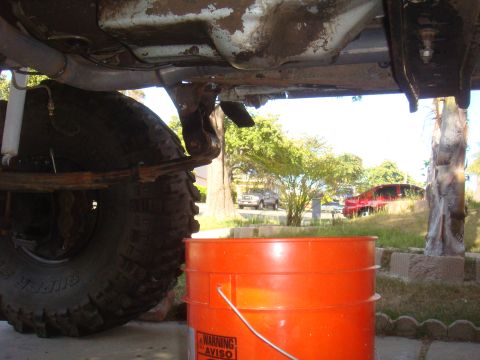Underside of a vehicle with a large tire and an orange bucket. Other vehicles visible in background