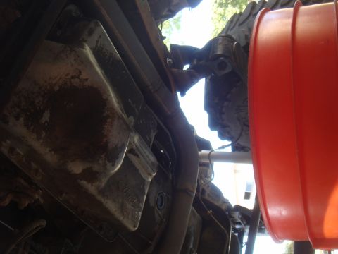 Underside of a vehicle with a rusty oil pan and exhaust pipe, next to a large orange funnel