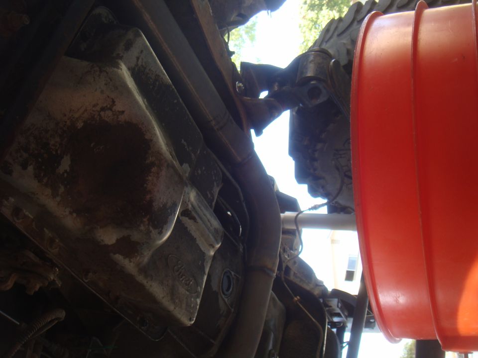Underside of a vehicle with a rusty oil pan and exhaust pipe, next to a large orange funnel