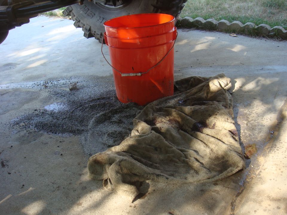 Orange bucket and stained rag on concrete, with part of a tire and suspension visible