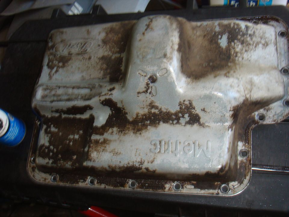 Ford oil pan with "Metric" stamped on it, covered in oil residue