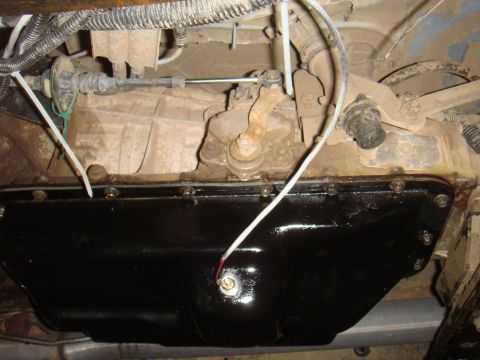 Underside view of a transmission pan and linkage assembly, with wiring and cables attached