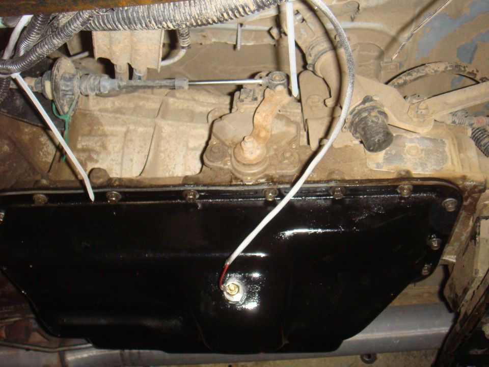 Underside view of a transmission pan and linkage assembly, with wiring and cables attached