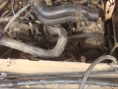 Engine bay with hoses, belts, alternator, and AC compressor visible