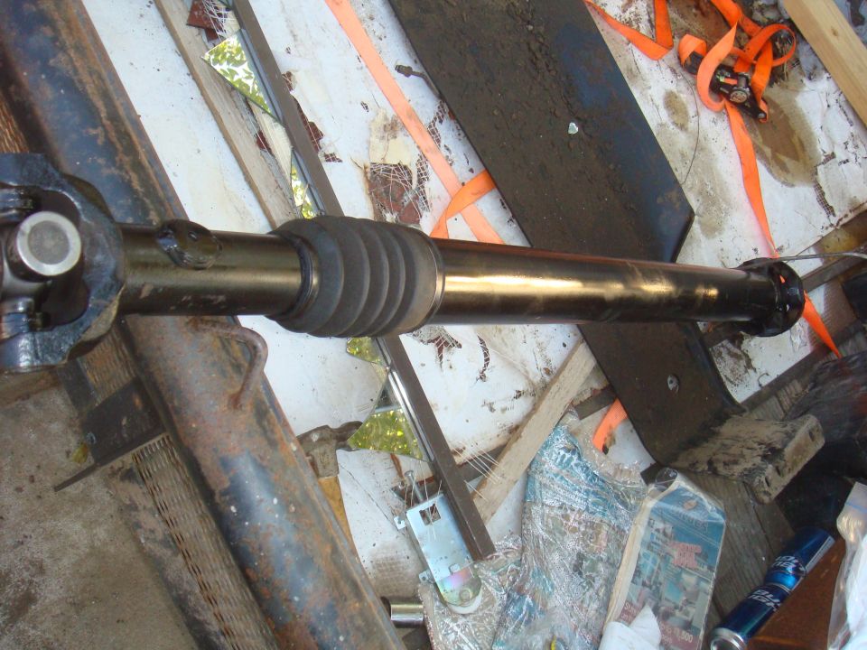 Driveshaft with U-joint and rubber boot, lying on a surface with straps and debris