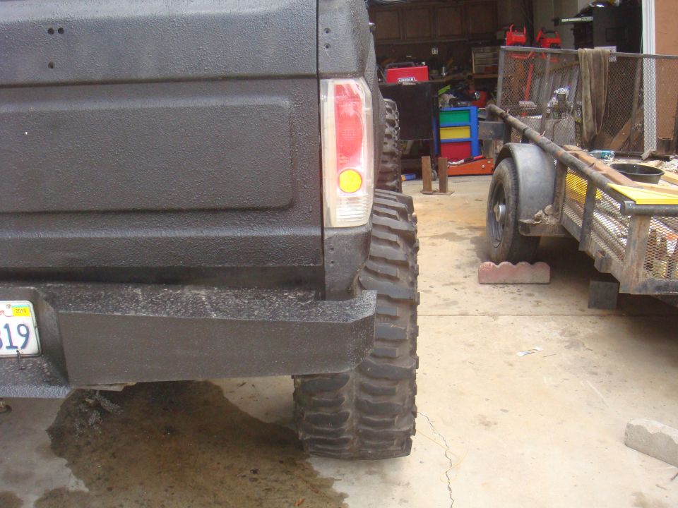 Rear of a black Ford Bronco with large off-road tires, parked next to a trailer in a garage