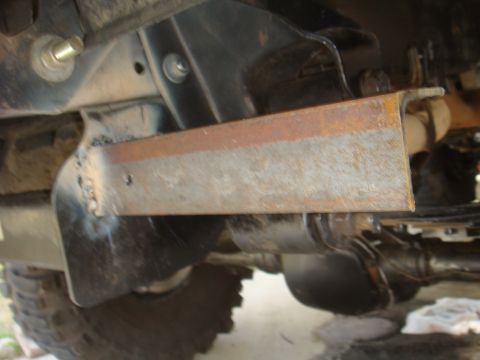 Close-up of rusted metal bracket welded to underside of vehicle frame, with tire visible