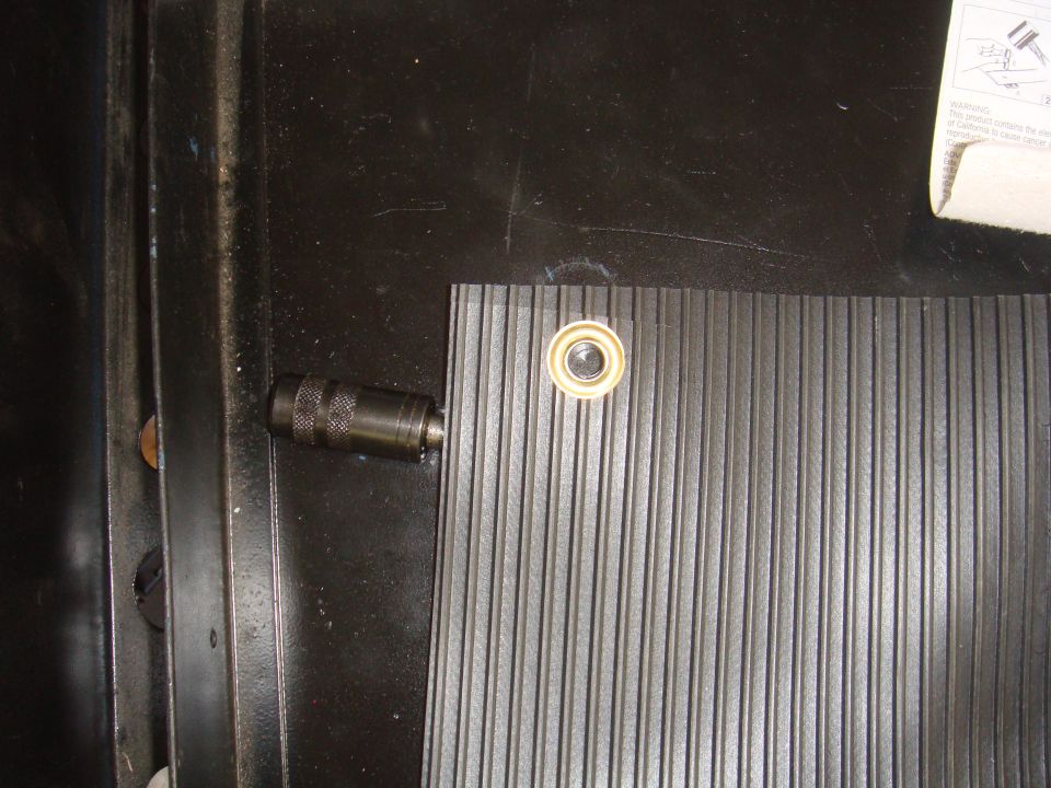 Close-up of a ribbed mat with a metal fitting and grommet in a dark vehicle interior. A document is partially visible