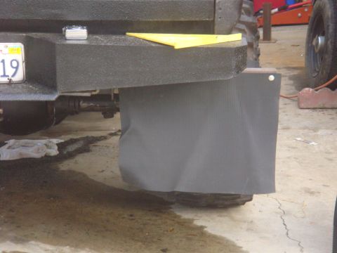 Black textured rear bumper with a license plate and a gray mud flap over a tire