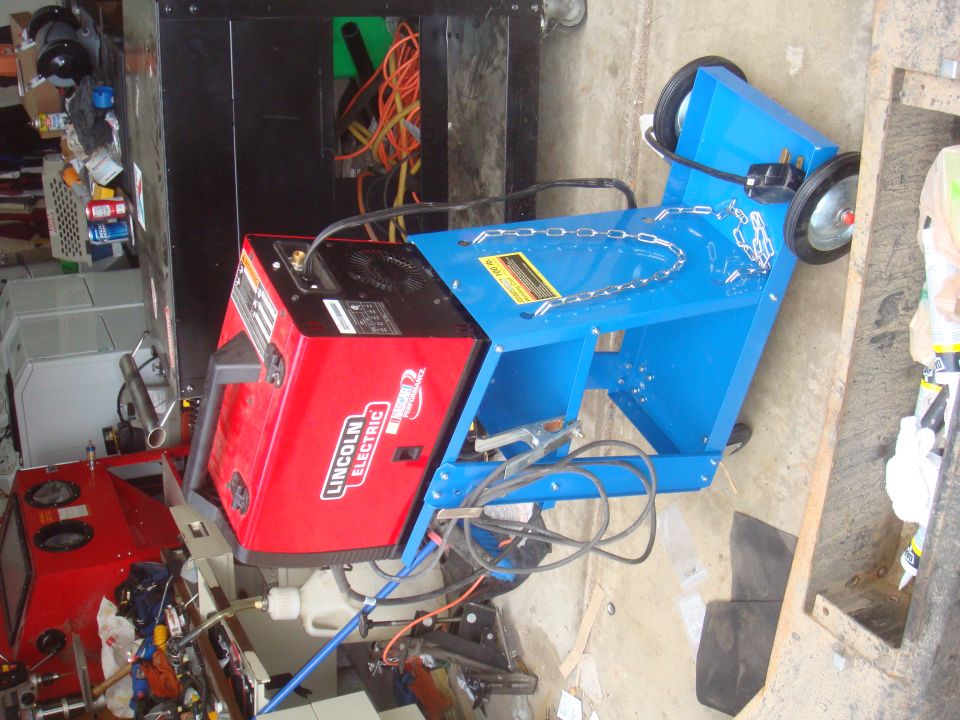 Red Lincoln Electric welder on a blue cart with wheels