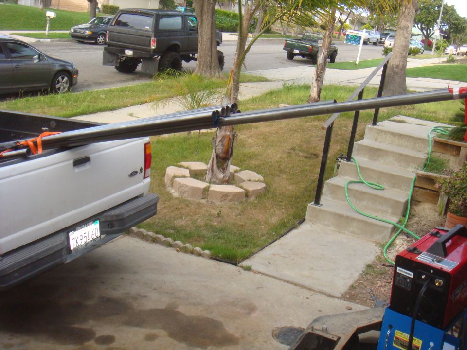 1992 Ford Bronco parked on street, viewed from rear of silver pickup truck carrying pipes