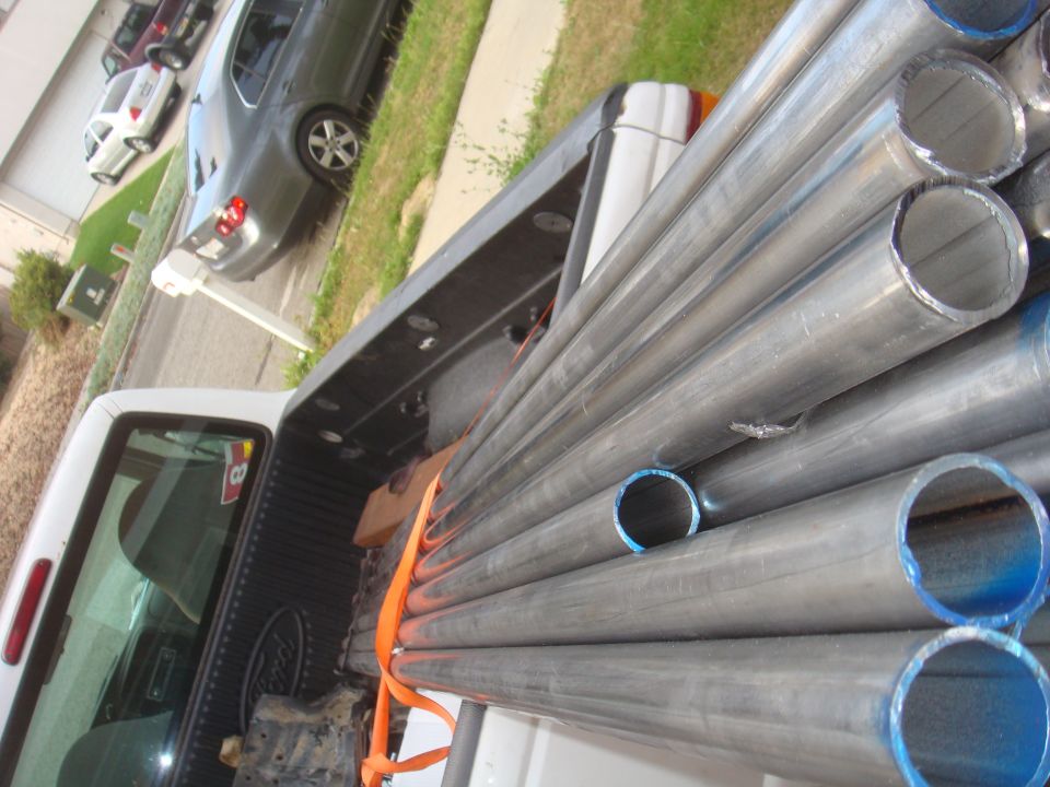 Truck bed loaded with metal pipes. Other cars parked in background
