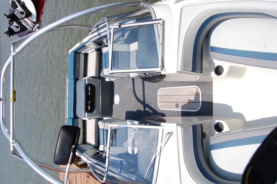 Boat interior with upholstered seating and windows, docked at a wooden pier