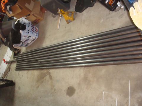 Pile of metal pipes on a concrete floor, with a laundry basket and boxes in the background
