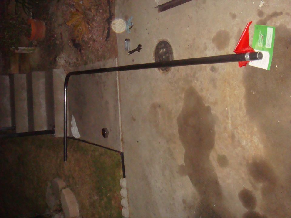 Metal pipe with red plastic and green packaging attached to one end, lying on concrete