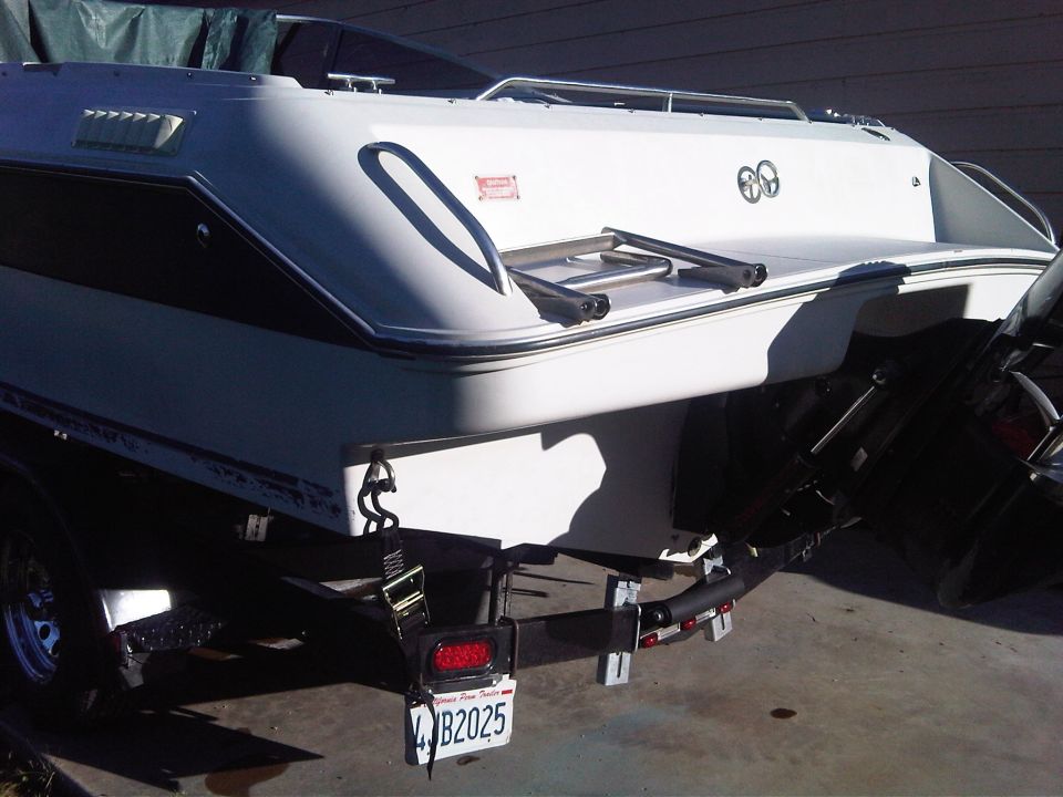 White and blue cabin cruiser boat on a trailer, rear view with boarding ladder