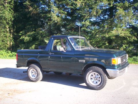 1990 Ford Bronco - A dark green 1990 Ford Bronco is parked outdoors on a sunny day.