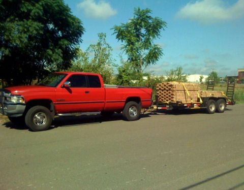 1989 Ford Bronco - A red pickup truck tows a trailer full of bricks on a sunny day.