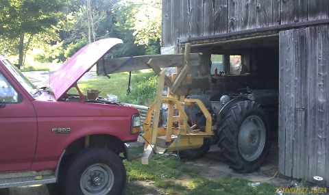 1985 Ford F-150 - A red Ford F-350 truck's engine compartment is visible as it is parked beside a tractor inside a barn.