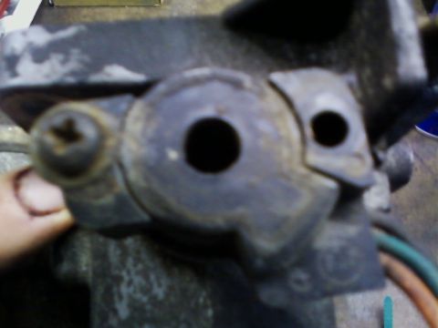 1990 Ford Bronco - Blurry close-up of a grimy cast aluminum throttle body held in a hand over a workbench, shot down the open throttle bore with the butterfly…