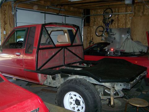 1988 Suzuki Samurai - A red flatbed truck with a custom metal cage is parked in a garage, alongside another vehicle.