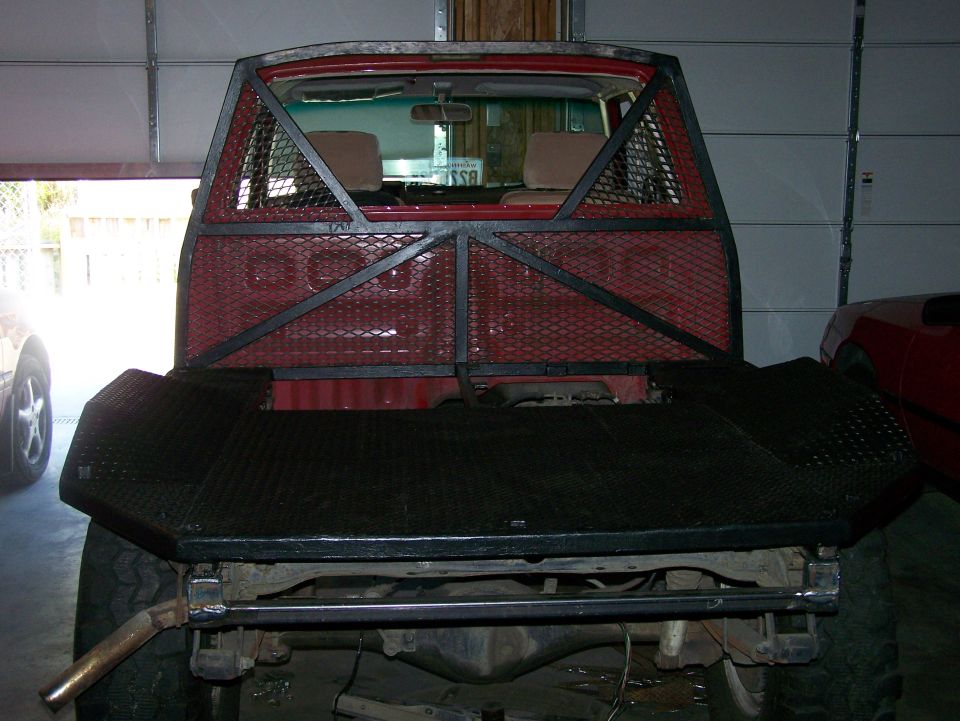 Rear view of a red truck with a custom metal cage over the bed and a large aftermarket bumper