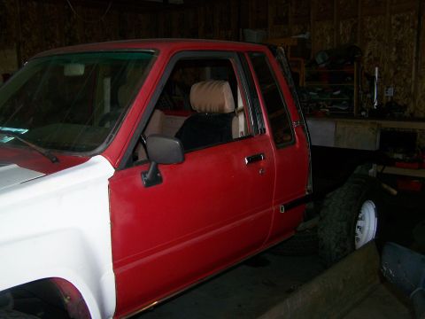 1988 Suzuki Samurai - A red pickup truck is parked inside a garage, showing its driver's side with a white fender.