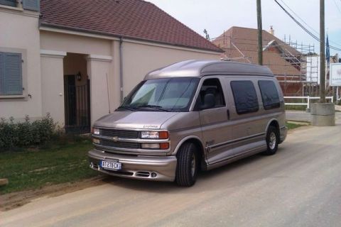 1991 Ford Crown Victoria - This Chevrolet Express van is parked on a dirt road with a house in the background.