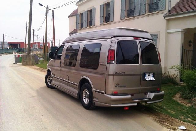 Tan van parked on a dirt road, viewed from the rear three-quarter angle