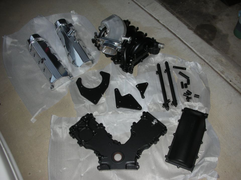 Engine parts including intake manifold, valve covers, and timing cover laid out on plastic sheeting