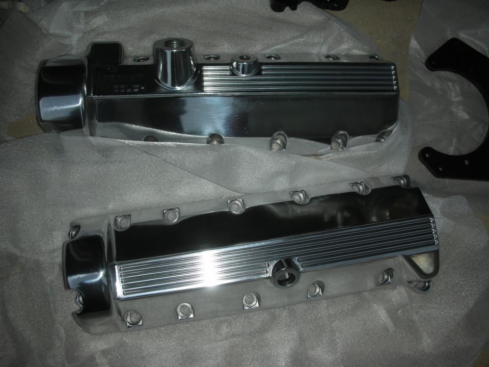 Two chrome valve covers with horizontal fins, one slightly above the other, resting on a soft surface