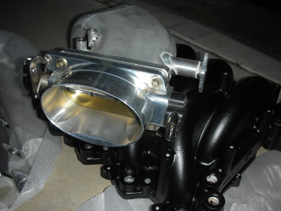 Close-up of a polished aluminum throttle body attached to a black intake manifold