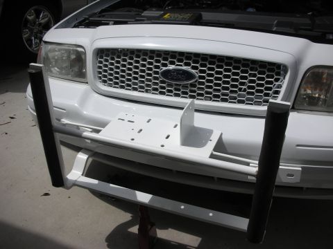 2004 Ford Crown Victoria - Close front view of a white Ford sedan with the hood raised, showing a white-painted push-bumper mounting bracket bolted to the frame horns…