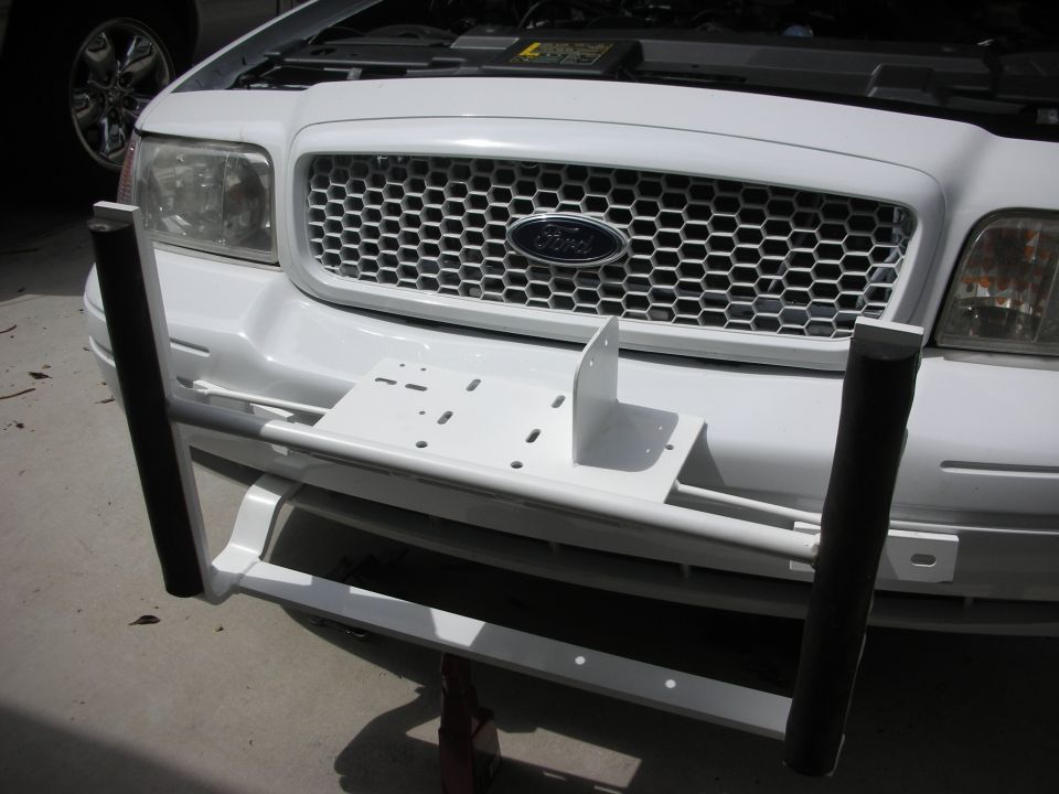 White-painted push bumper bracket mounted to the frame of a white Ford sedan, hood open